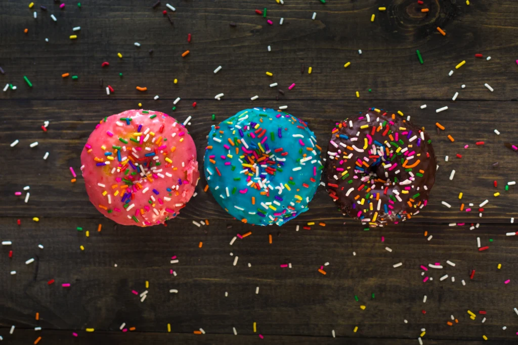 3 gekleurde donuts die op tafel liggen, als symbool voor emotie-eten. 